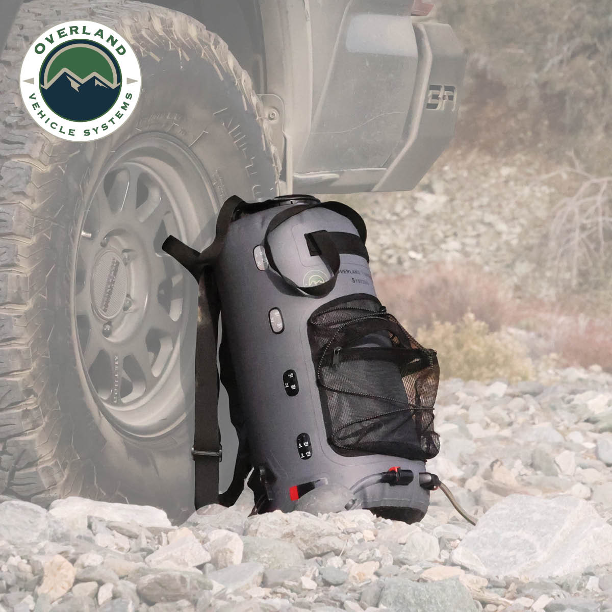 Portable shower on a rocky terrain with Overland Vehicle Systems logo.