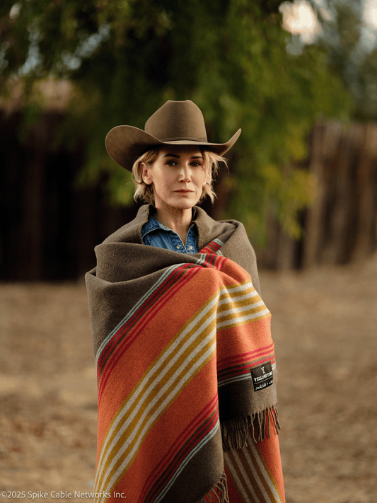 Person wearing a cowboy hat and wrapped in a colorful blanket in a natural setting
