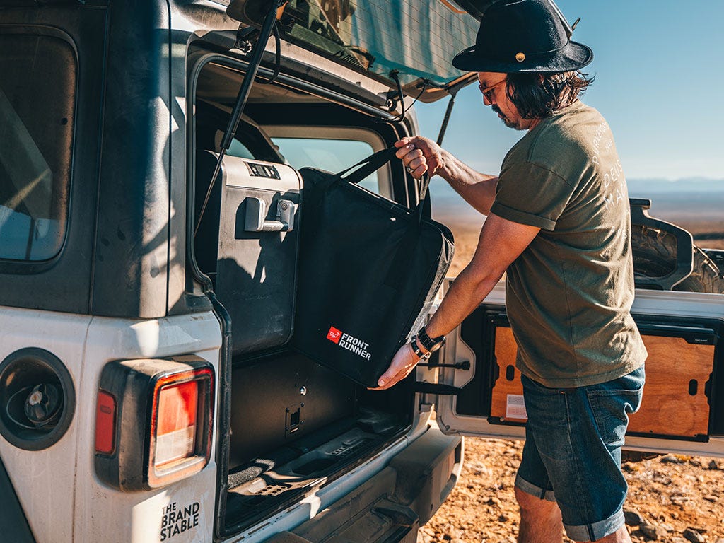 Man opening the back of a vehicle with a 'Brand Front Runner"' bag inside, in a desert setting.