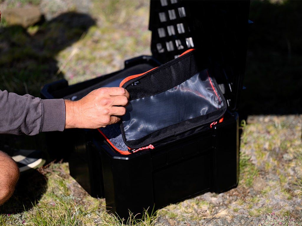 Person opening a black tool box with orange accents outdoors.