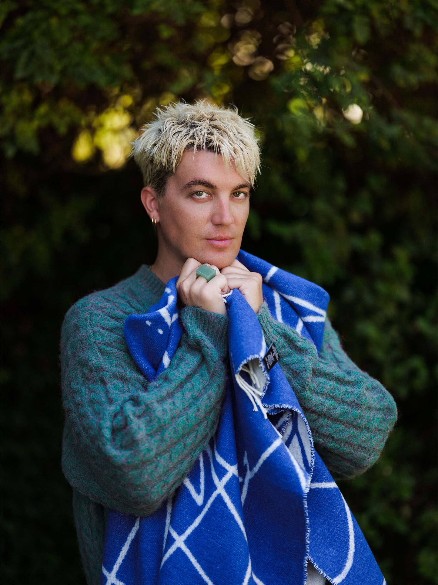 Person wearing a green sweater and blue patterned scarf against a blurred natural background