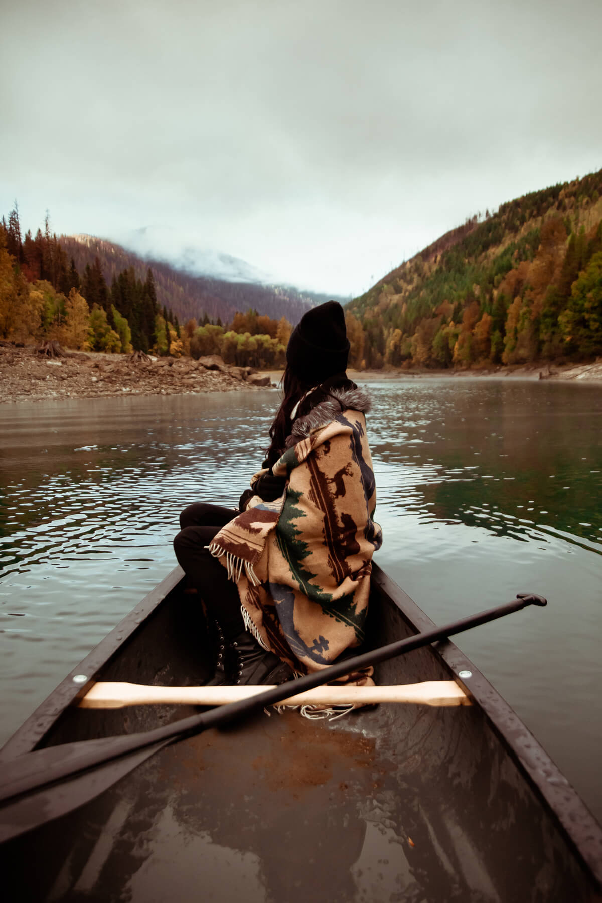 Person in a canoe on a calm lake with mountains in the background