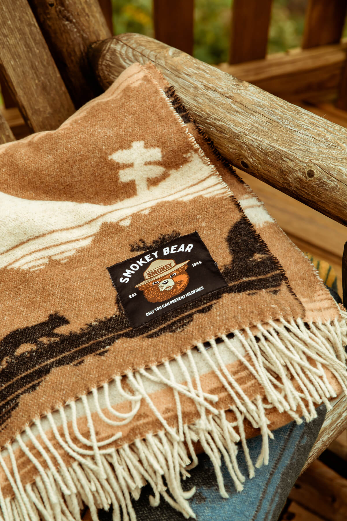 Woven blanket with fringes and a Smokey Bear label on a wooden surface