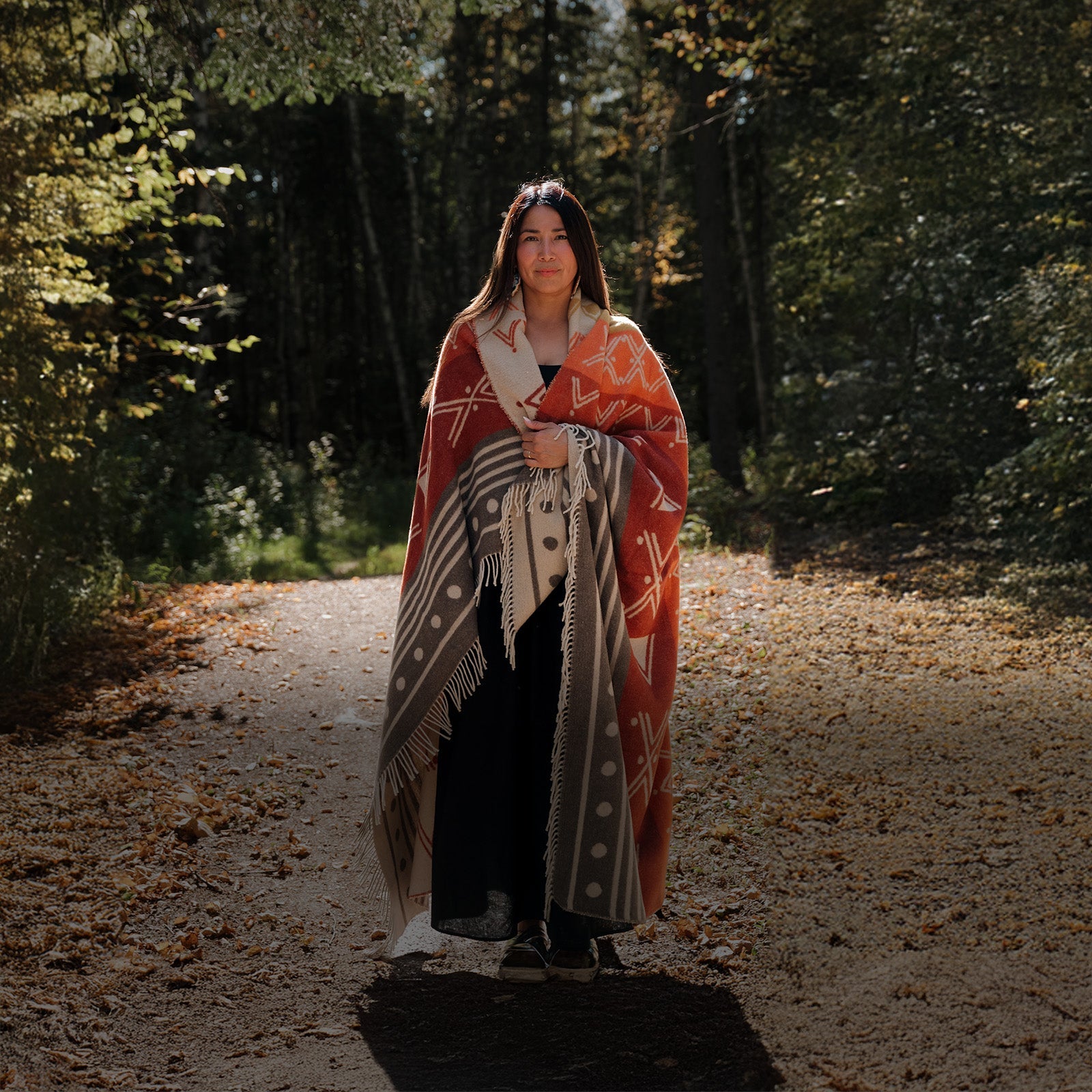 Woman wrapped in a patterned blanket standing on a forest path