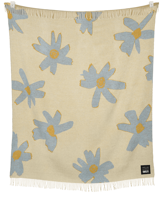Beige blanket with blue floral patterns and white fringe on a black background