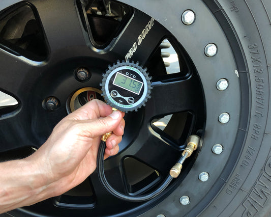 Hand using a digital tire pressure gauge on a car tire