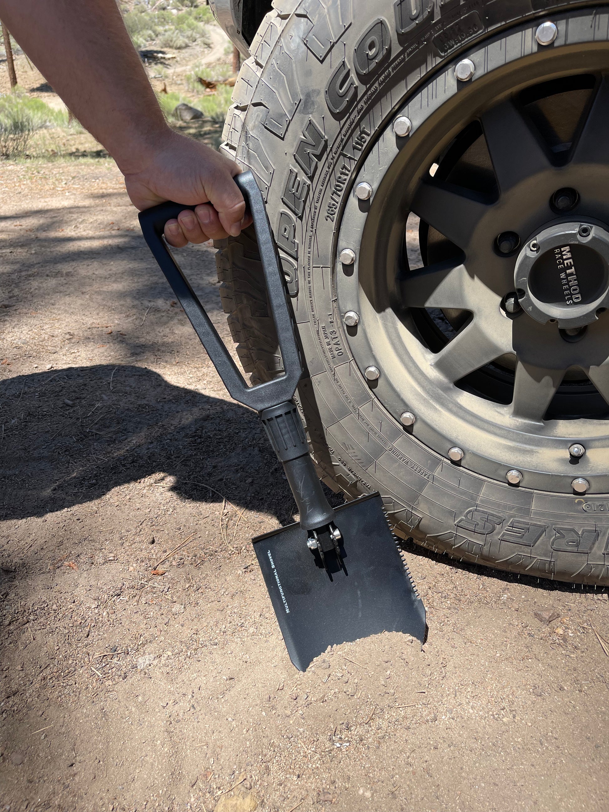 Person using a folding spade next to a tire on a road