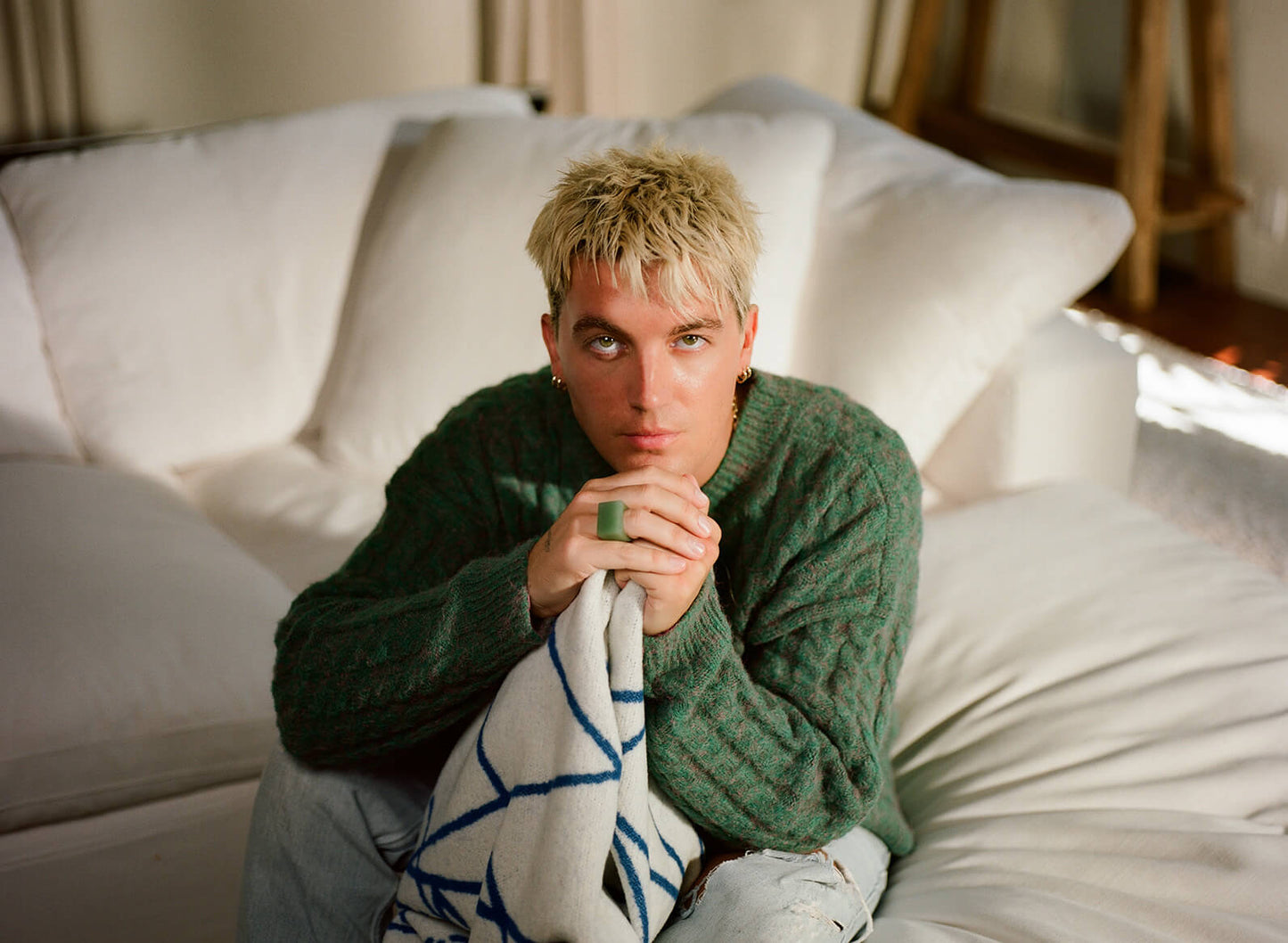 Man sitting on a couch holding a blanket, wearing a green sweater.