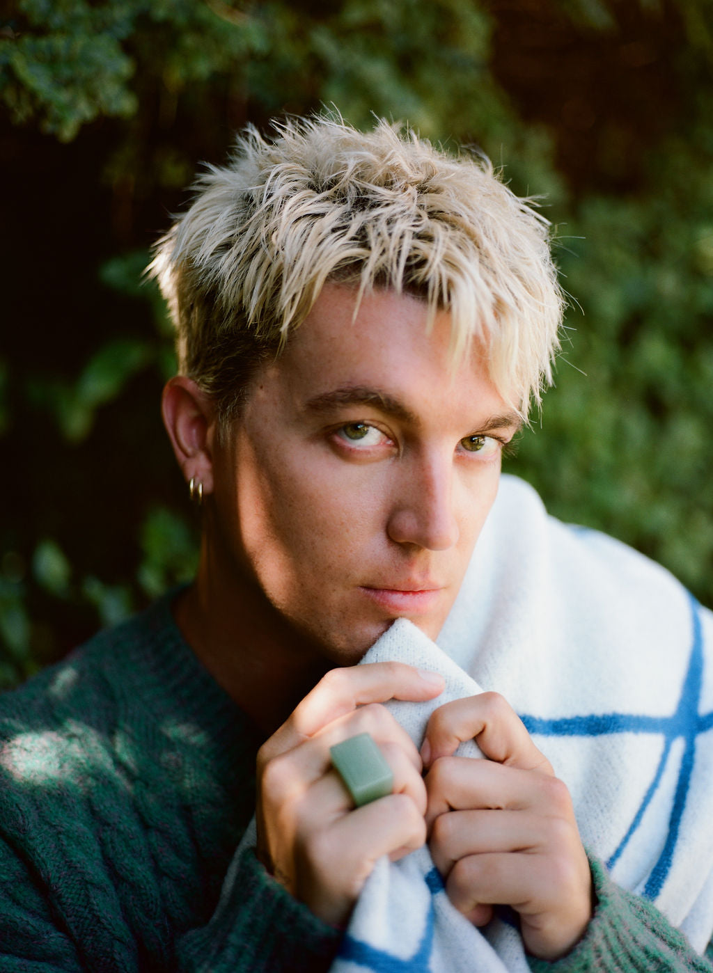 Person with blonde hair holding a towel, surrounded by greenery