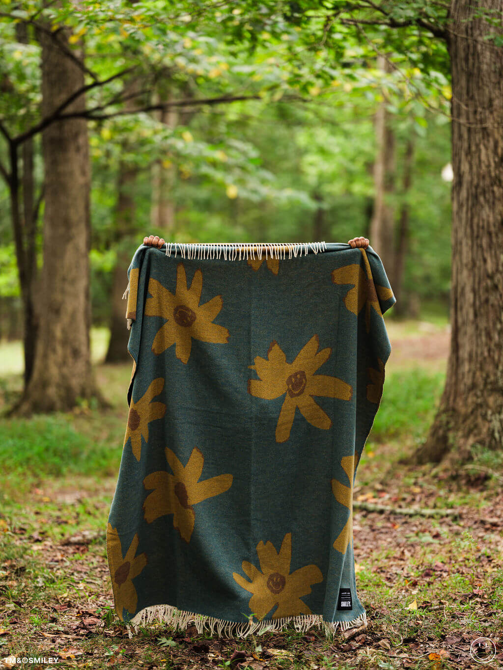 Green blanket with yellow floral patterns held up in a forest setting