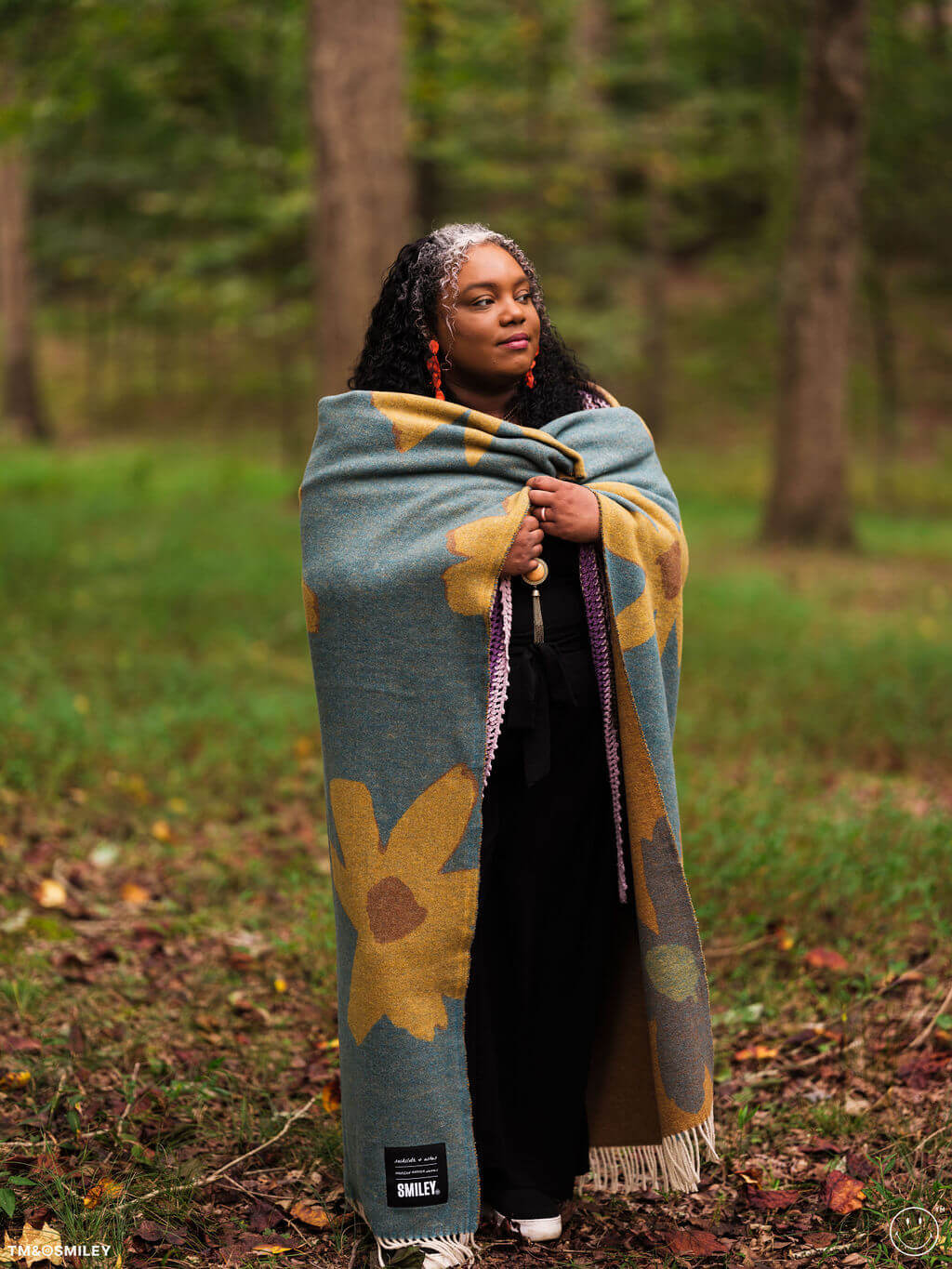 Person wrapped in a patterned blanket standing in a forest
