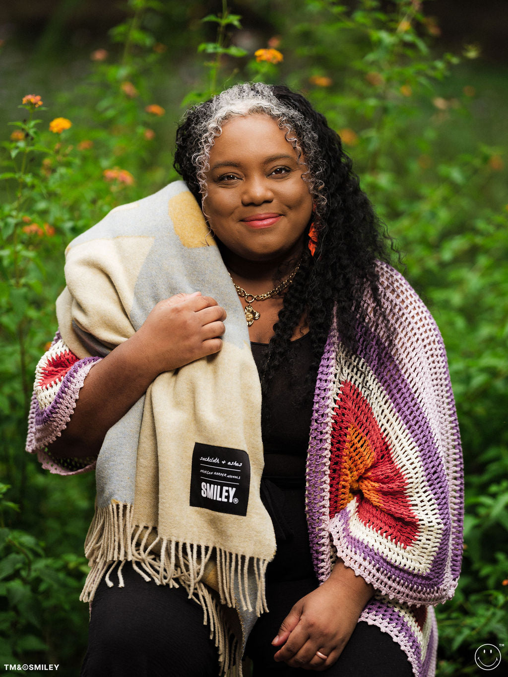 Woman wearing a colorful crocheted shawl with a brand label in a natural setting
