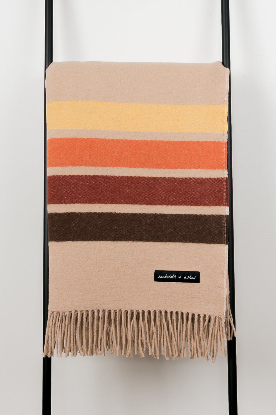 Striped blanket with fringes on a ladder against a white background