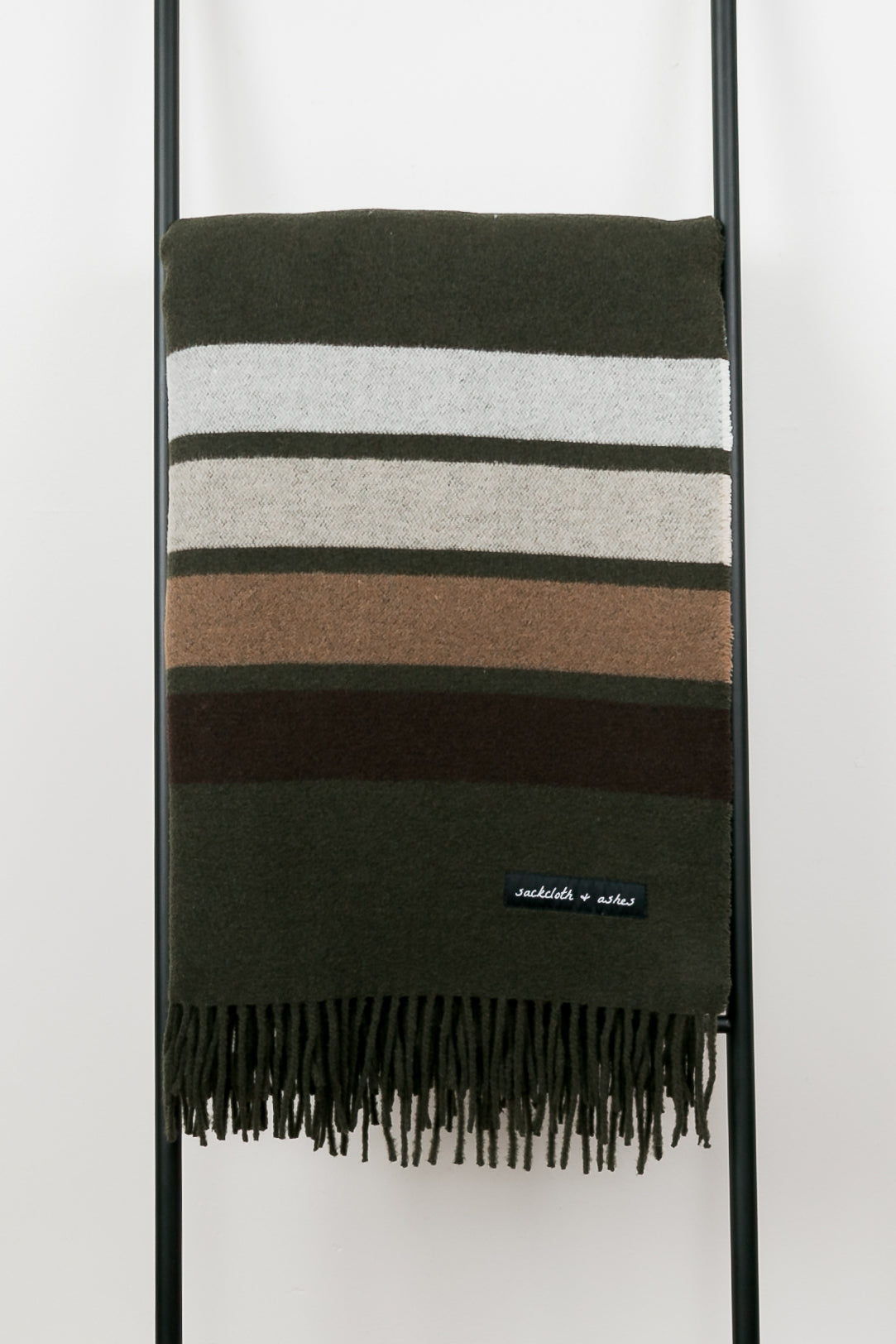 Striped blanket with fringes on a black stand against a white background