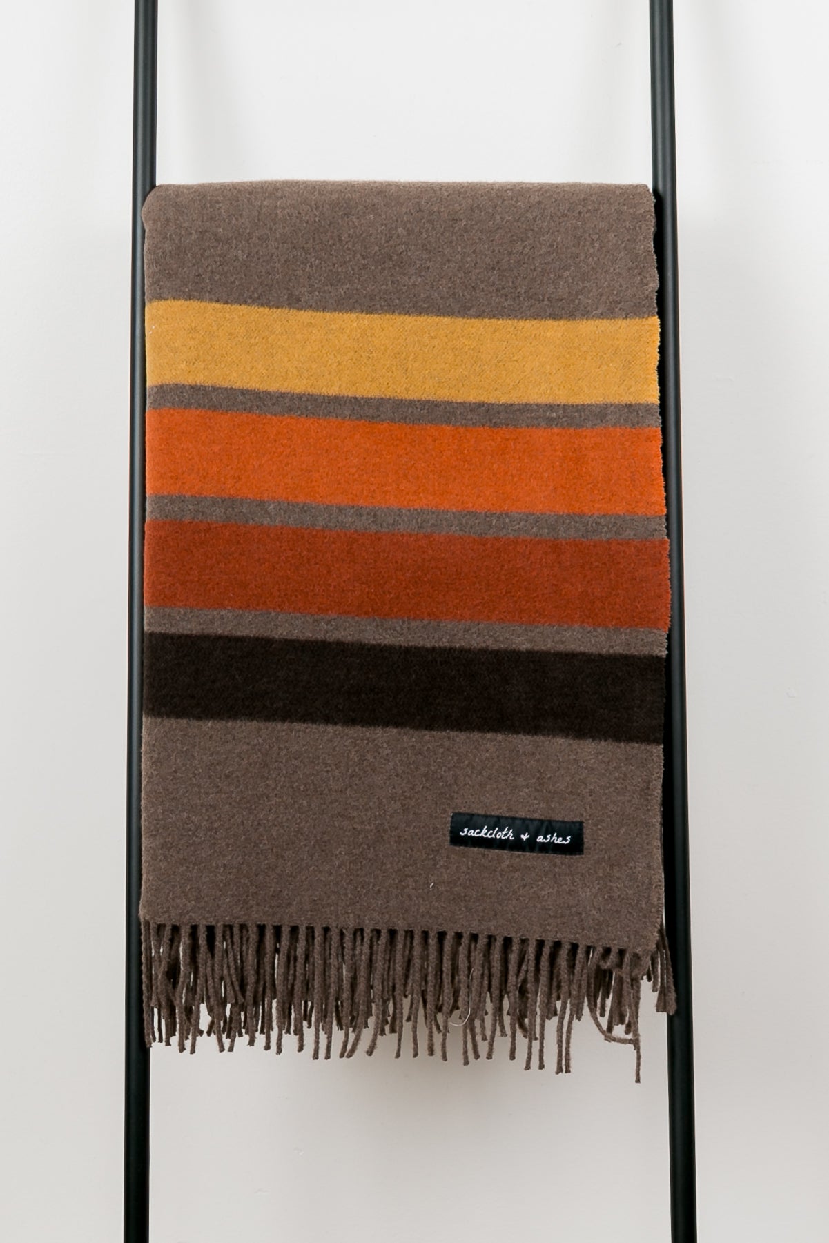 Striped blanket with brown, orange, and black colors on a ladder against a white background