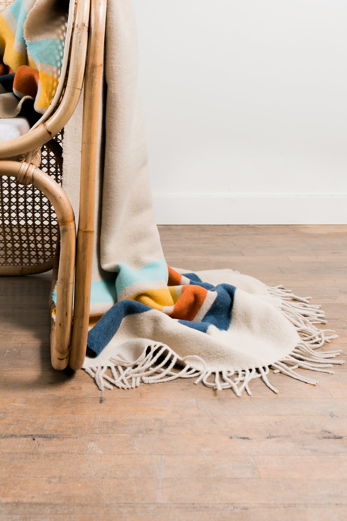 Colorful blanket draped over a wicker chair on a wooden floor.
