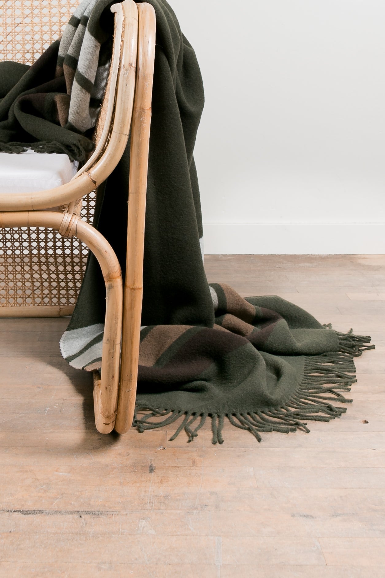 Green blanket draped over a wicker chair on a wooden floor.
