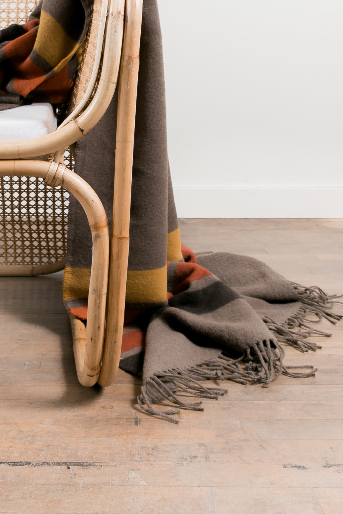 Textured blanket draped over a wicker chair on a wooden floor.