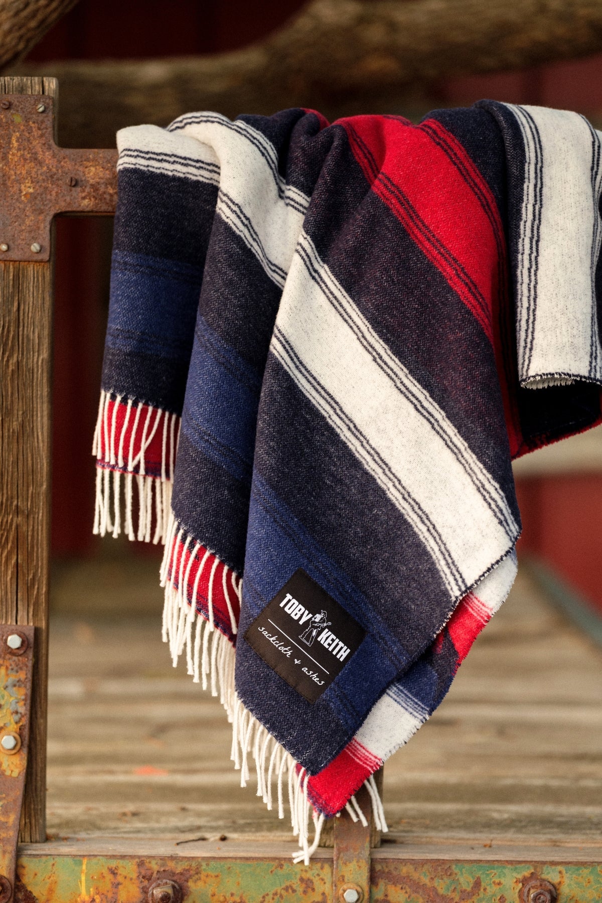 Striped blanket with fringes on a wooden surface, featuring a brand label.