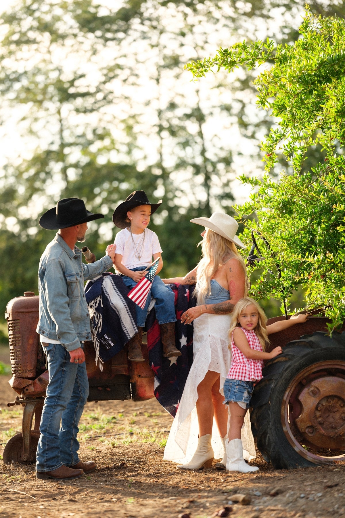 Family with children in cowboy hats on an old tractor outdoors