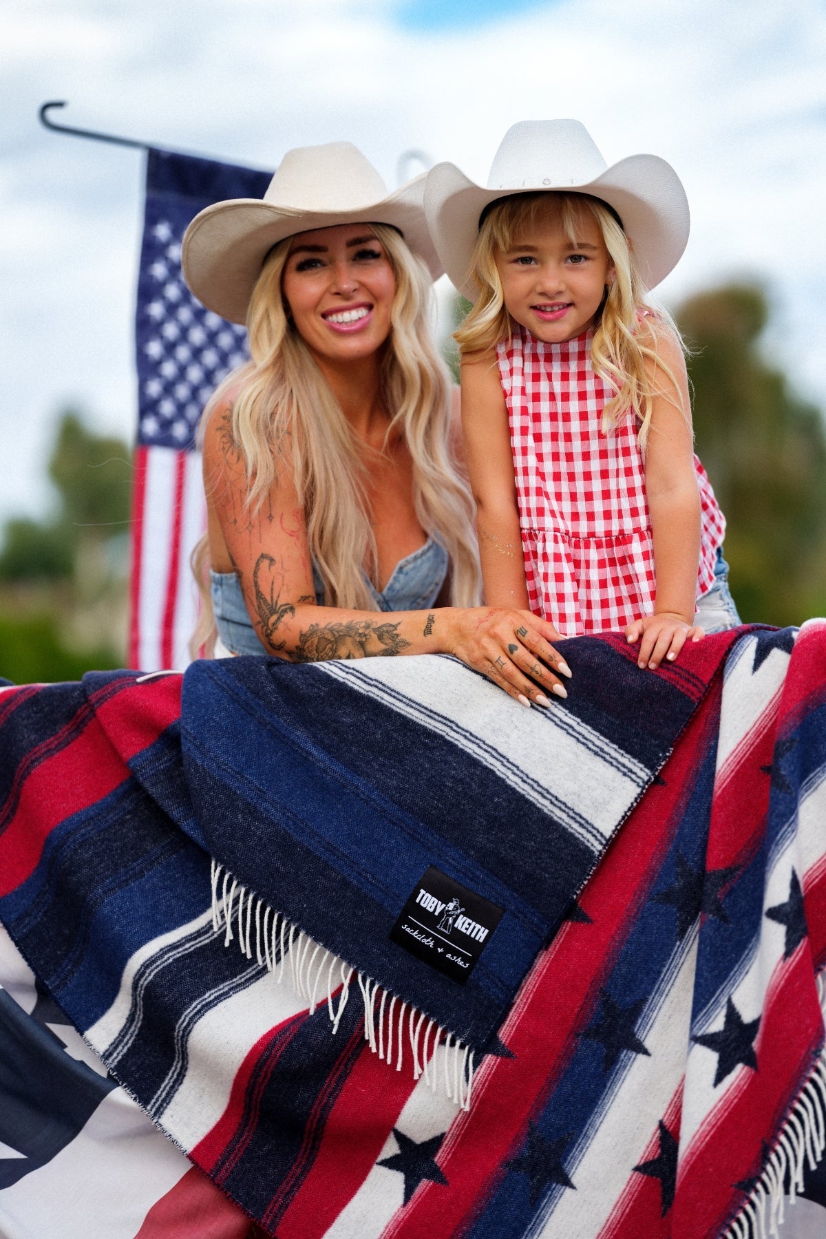 Woman and child sitting on a blanket with an American flag design, wearing cowboy hats.