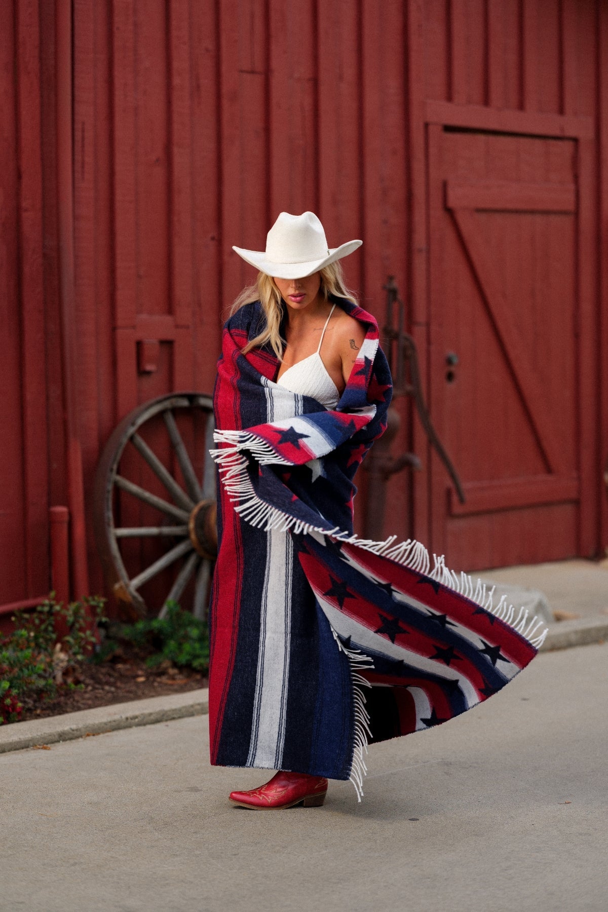 Woman in a colorful coat and cowboy hat standing in front of a red barn.