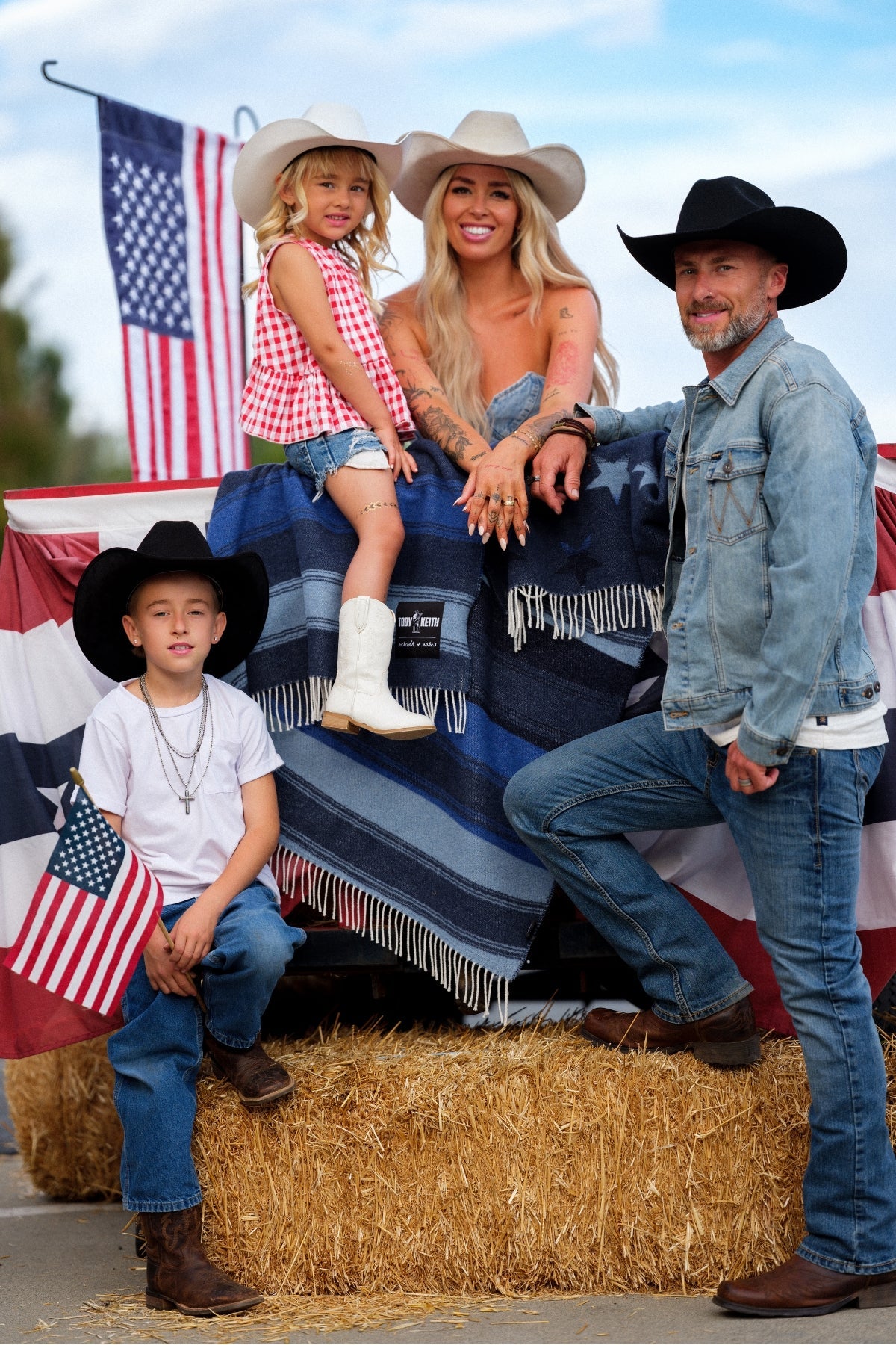 Family of four posing on a hay bale with American flags in the background