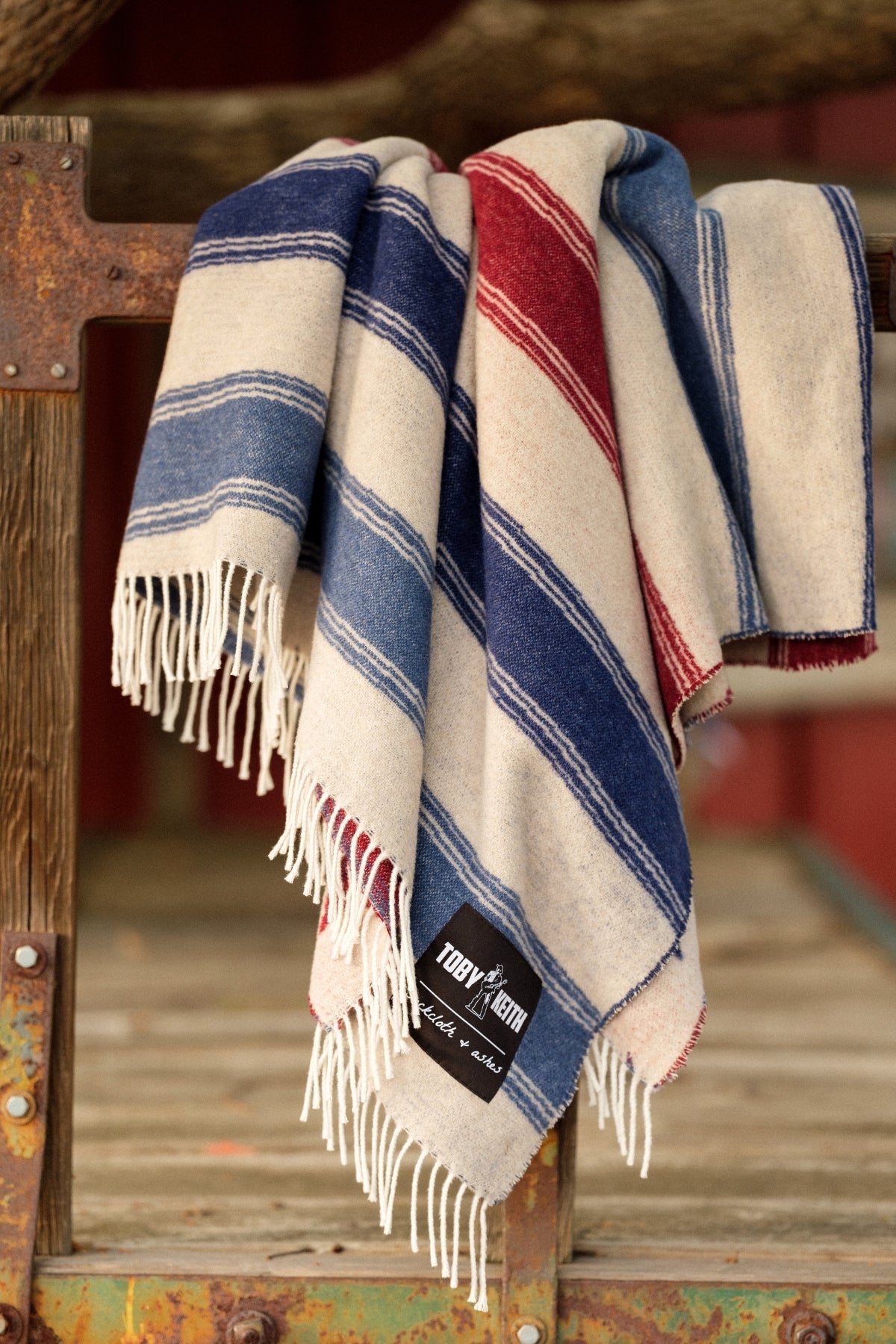 Striped blanket with fringes draped over a wooden surface, featuring a brand label.