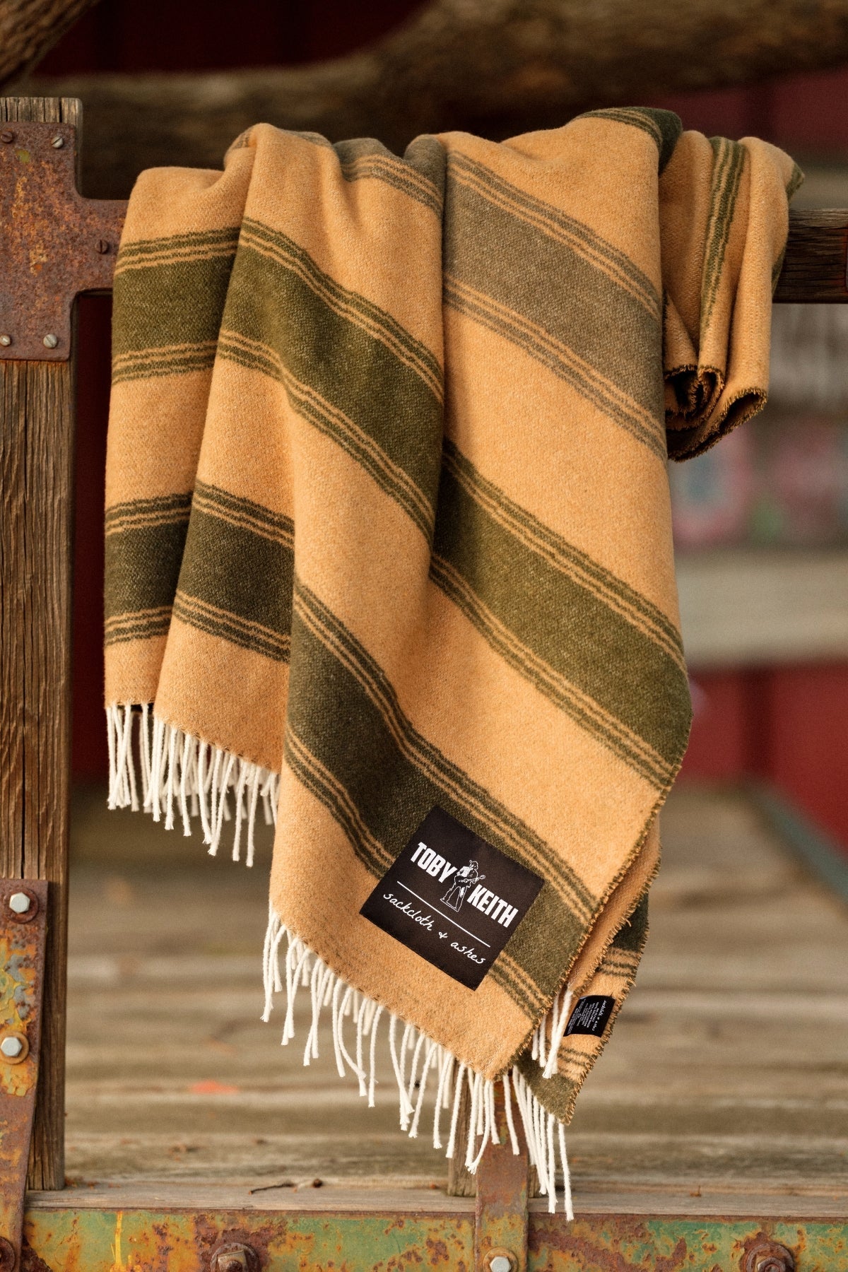 Striped blanket with fringes on a wooden surface, featuring a brand label.