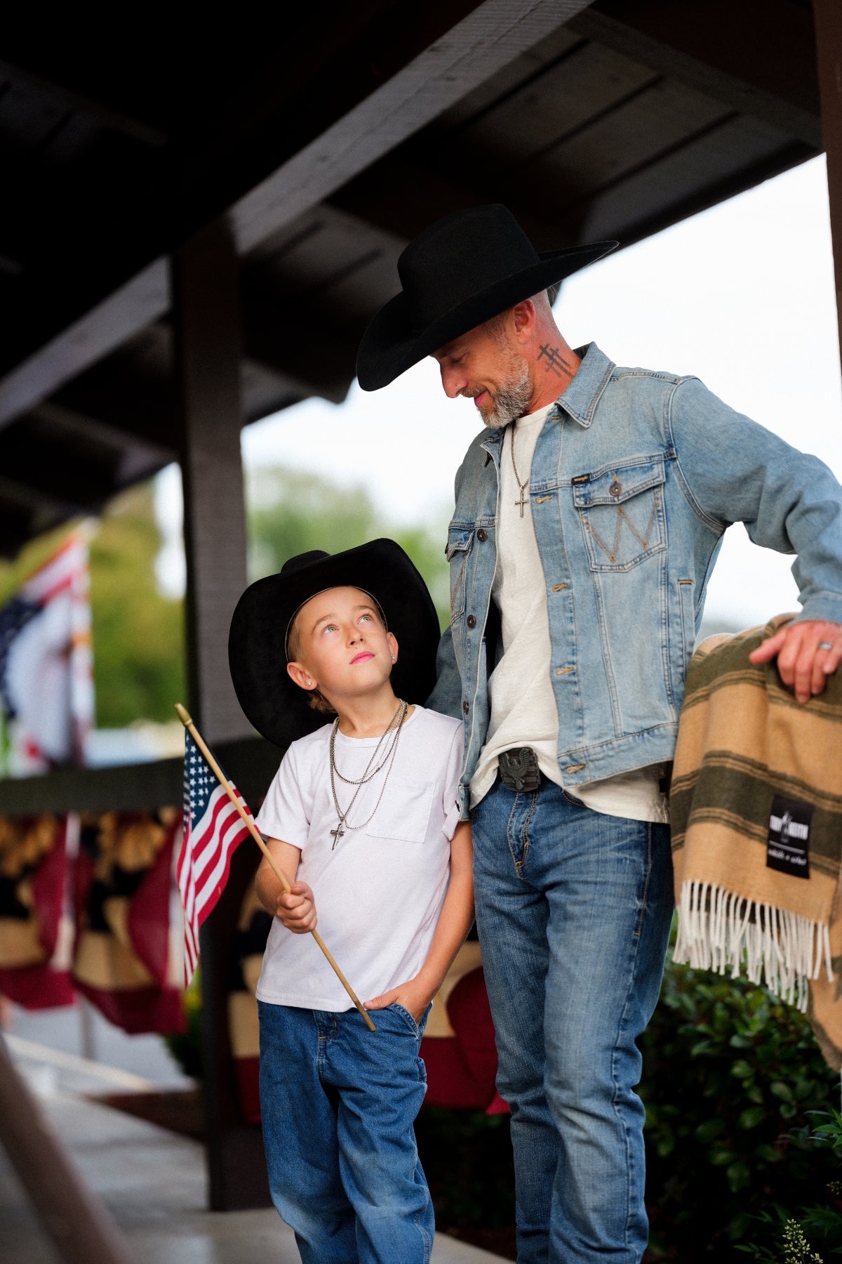 Man and child in cowboy hats with an American flag, standing outdoors.