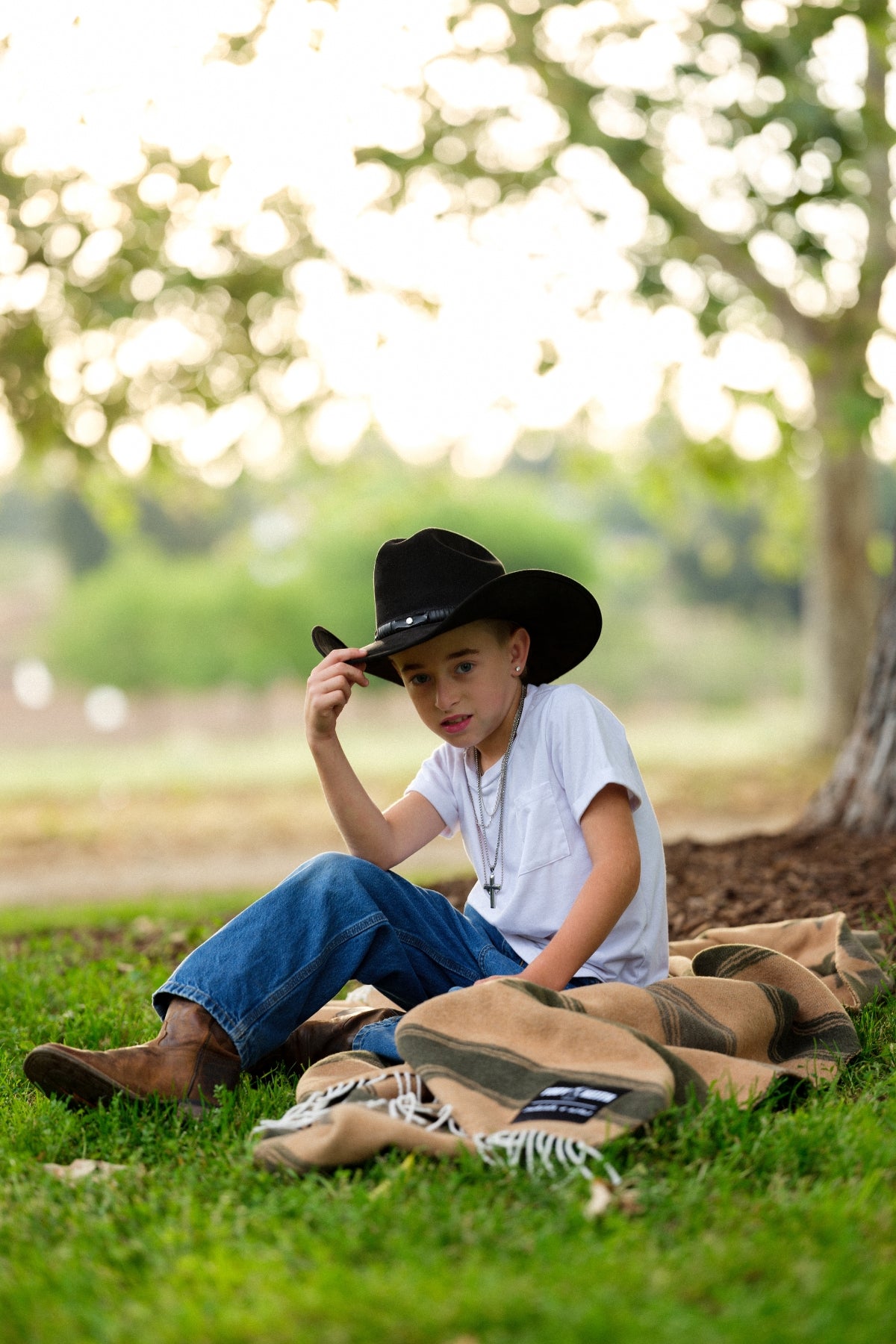 Child wearing a cowboy hat sitting on grass with a blanket