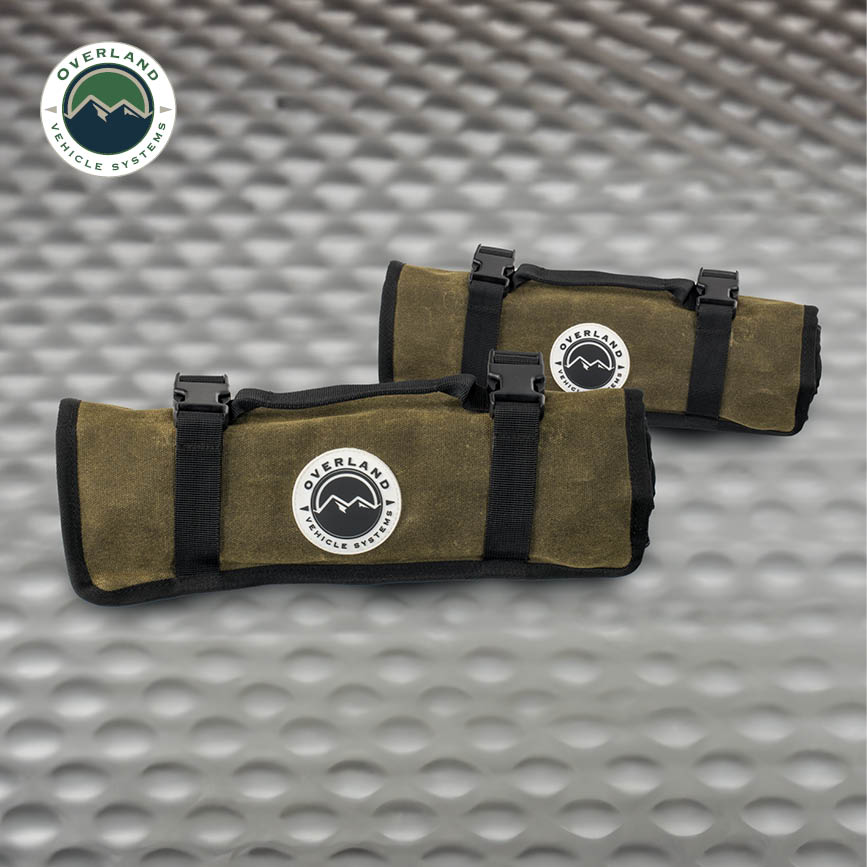 Two olive green roll bags with black straps on a textured metal surface, featuring the Overland Vehicle Systems logo.