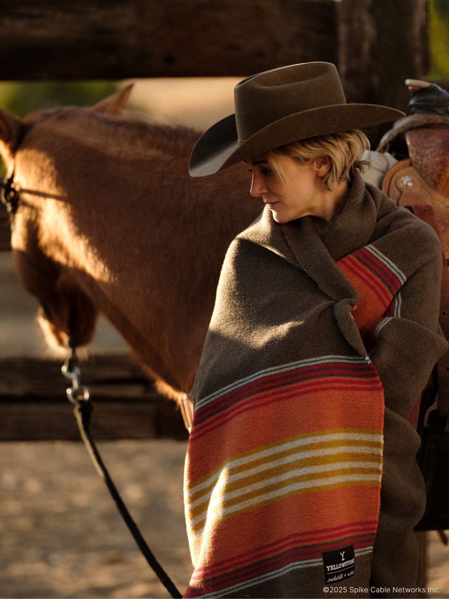 Woman in a cowboy hat and striped poncho standing next to a horse