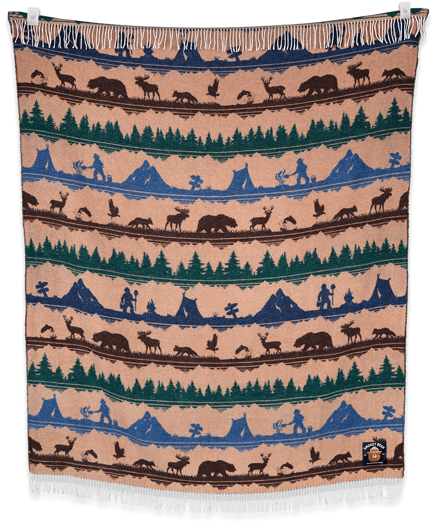Woven blanket with nature-themed design featuring animals, trees, and mountains on a beige background.