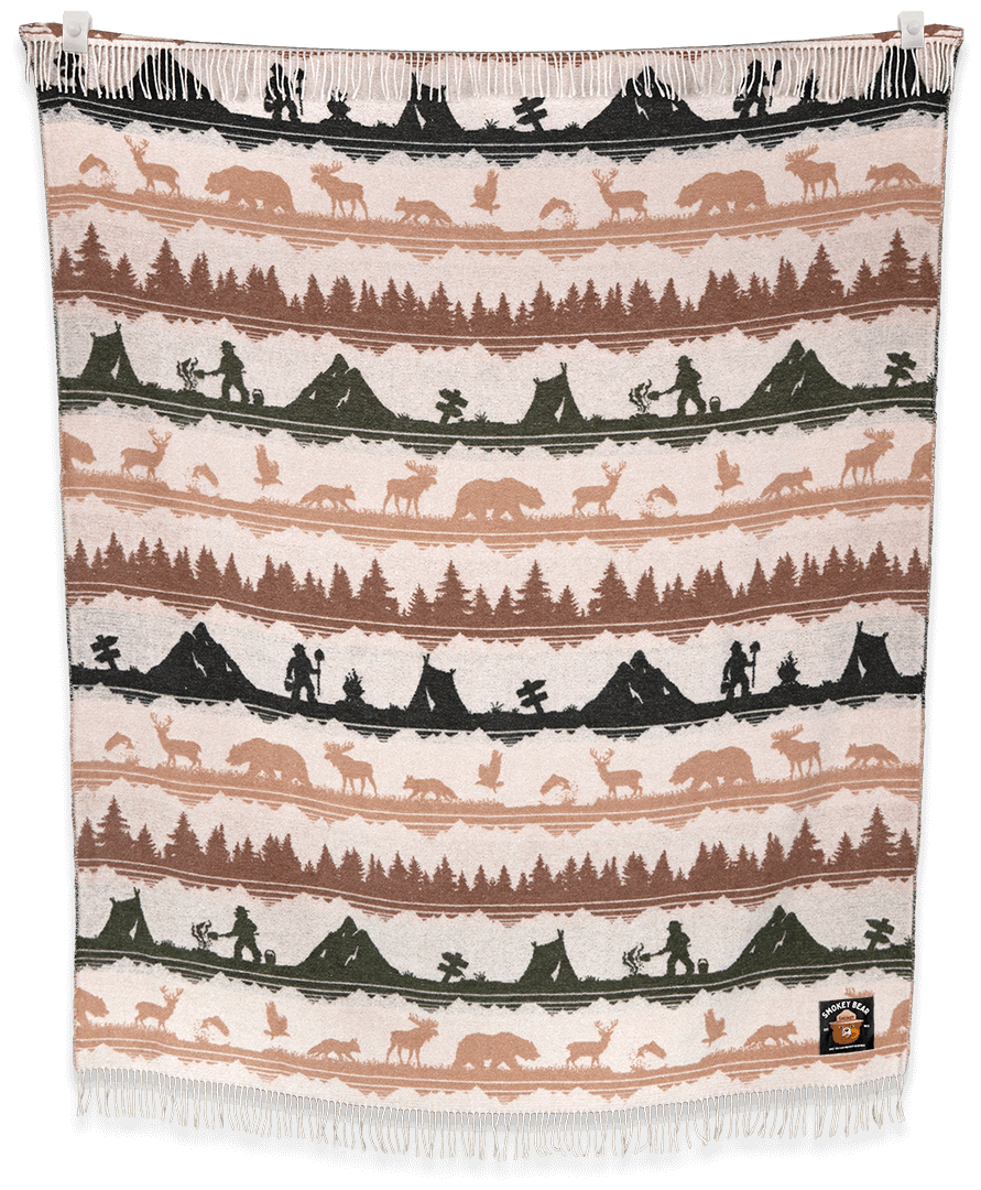 Woven blanket with nature-themed design featuring trees, animals, and people on a black background.