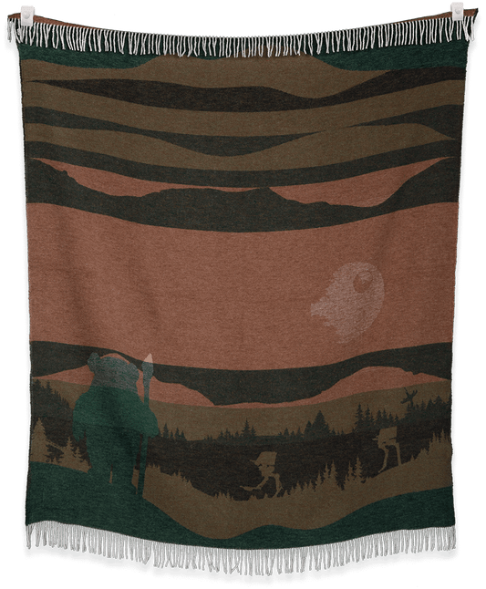 Woven blanket with a landscape design featuring a bear and trees, hanging on a black background.