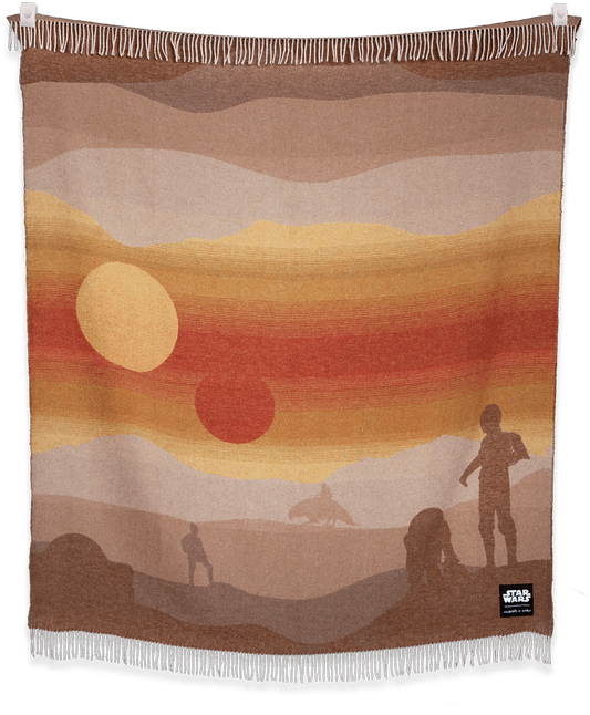 Woven blanket with desert landscape design featuring people, animals, and a sunset.