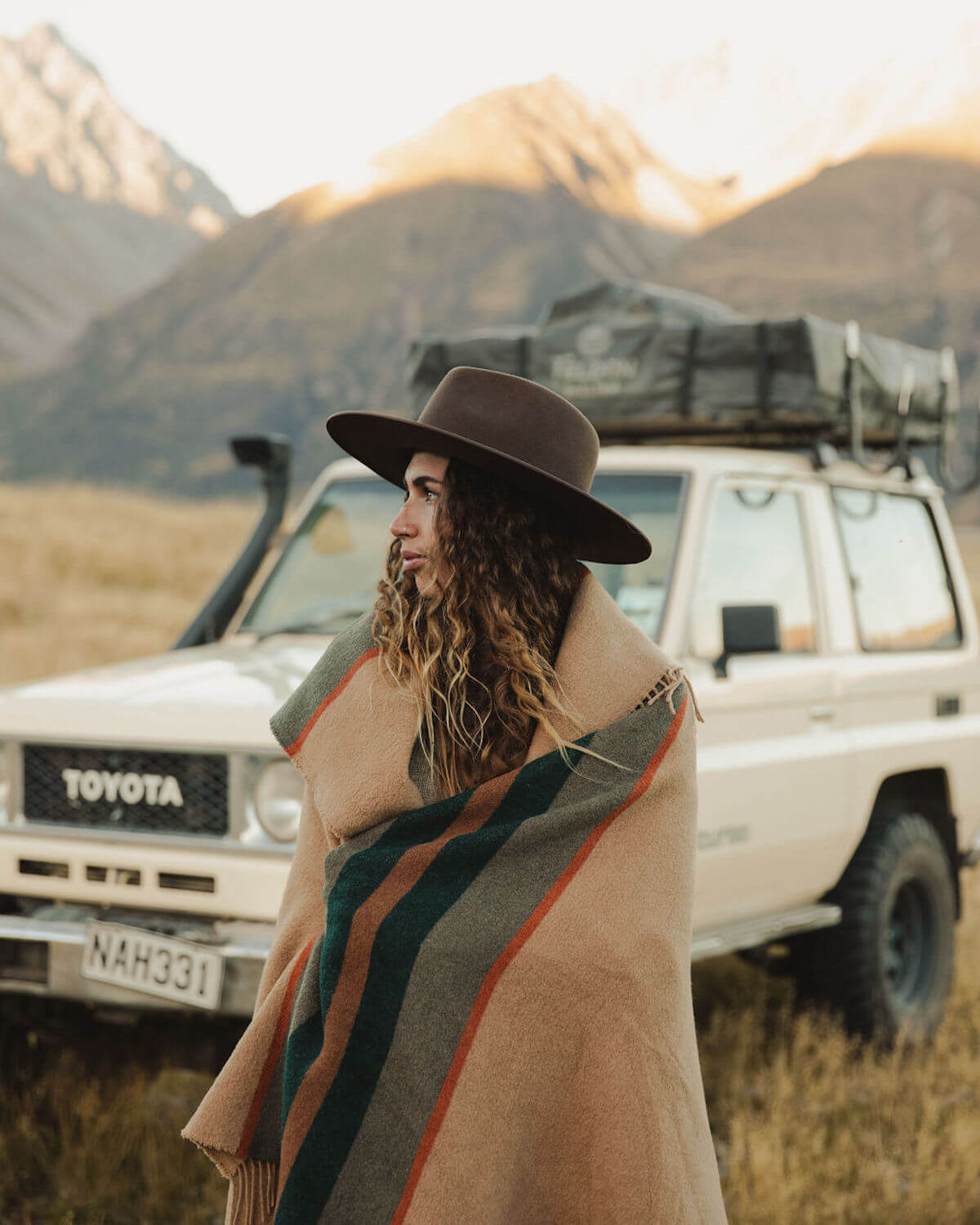 Person wrapped in a blanket standing in front of a Toyota vehicle with mountains in the background