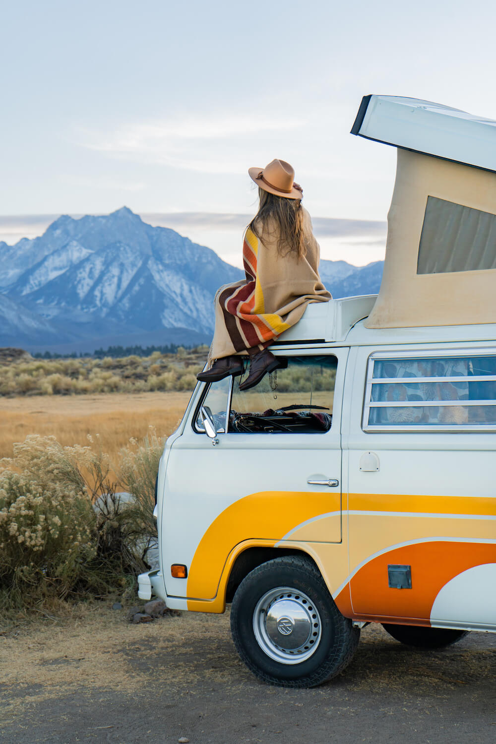 Person sitting on a camper van with mountains in the background