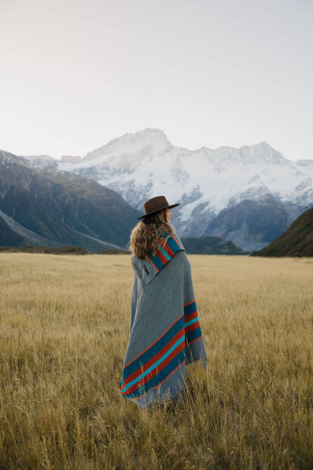 Person wrapped in a colorful blanket standing in a field with mountains in the background