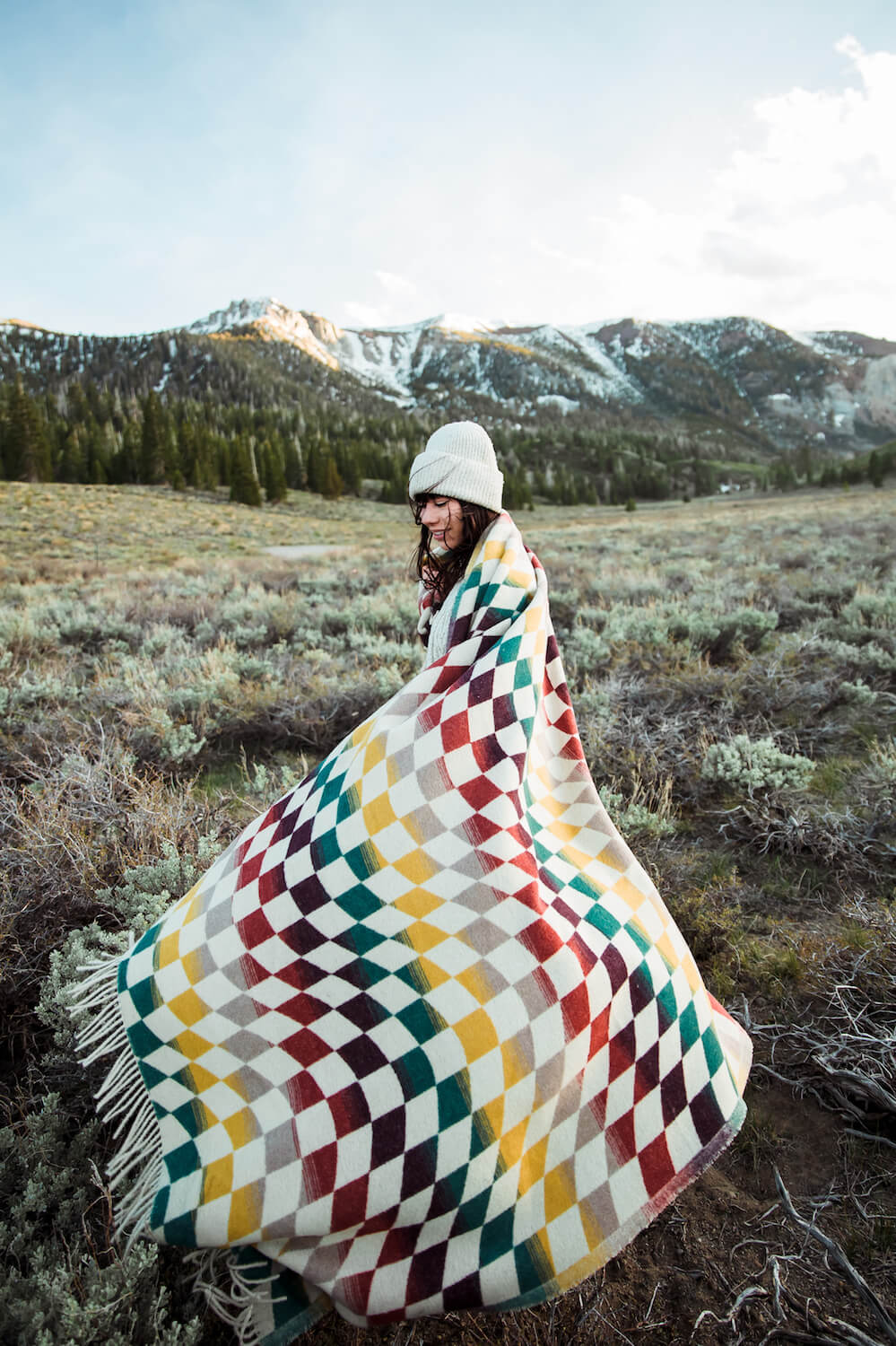 Person wrapped in a colorful checkered blanket in a mountainous landscape