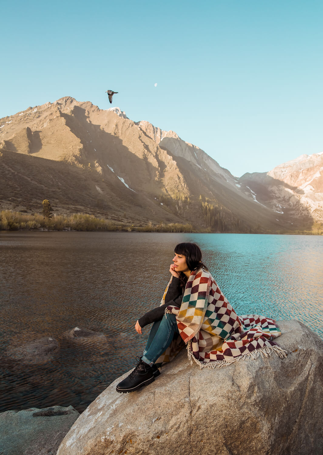 Person sitting on a rock by a lake with mountains in the background
