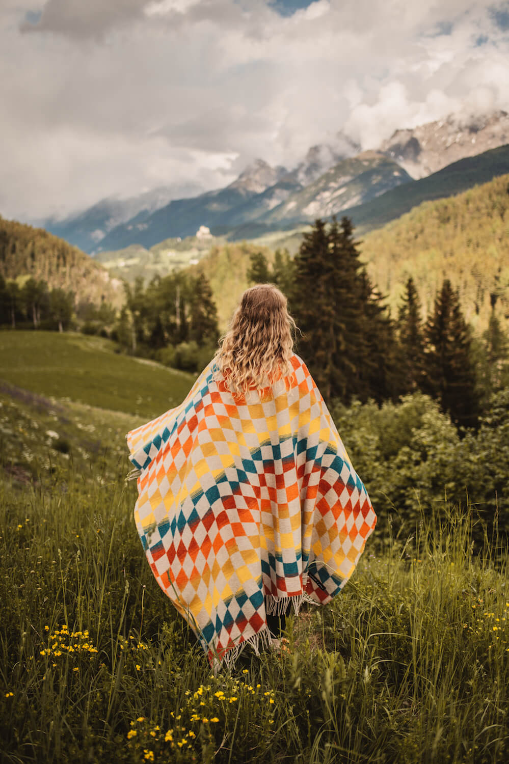 Person wrapped in a colorful blanket standing in a mountainous landscape