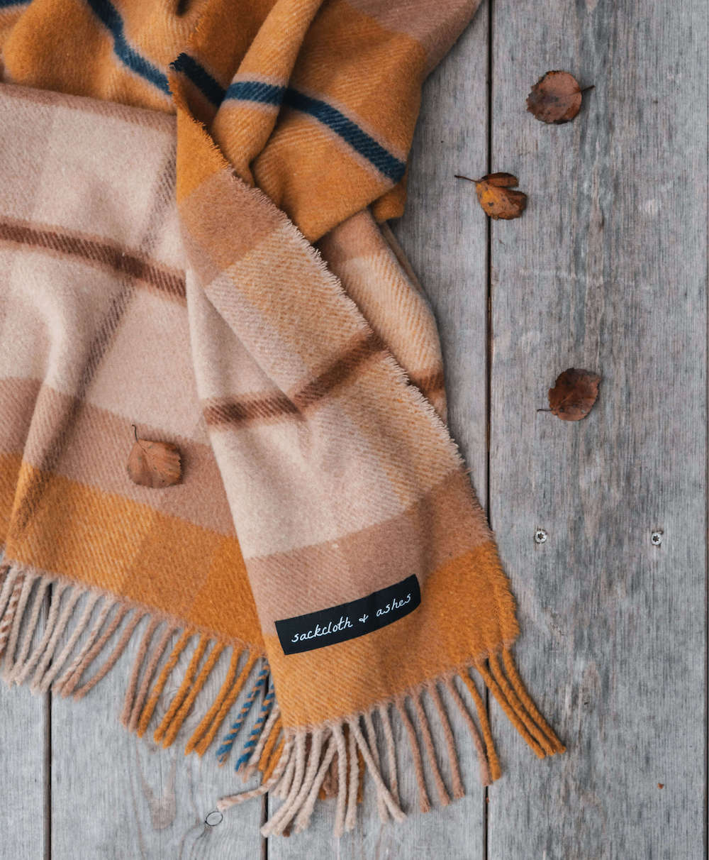 Plaid blanket with fringes and a brand label on a wooden surface