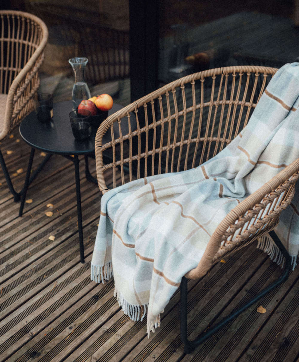 Wicker chair with a plaid blanket on a wooden deck