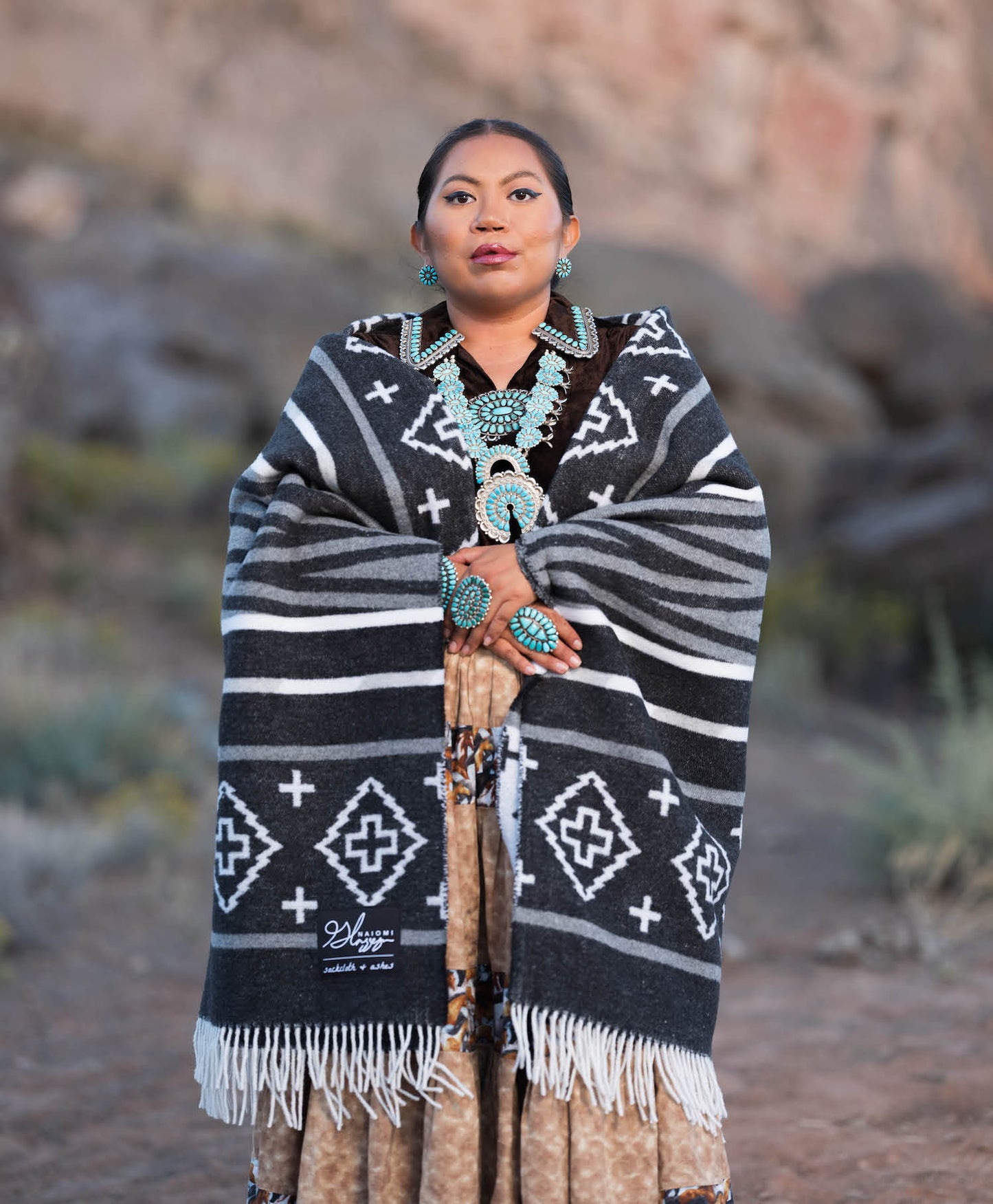Woman wearing a black and white patterned shawl with turquoise jewelry in a natural setting.