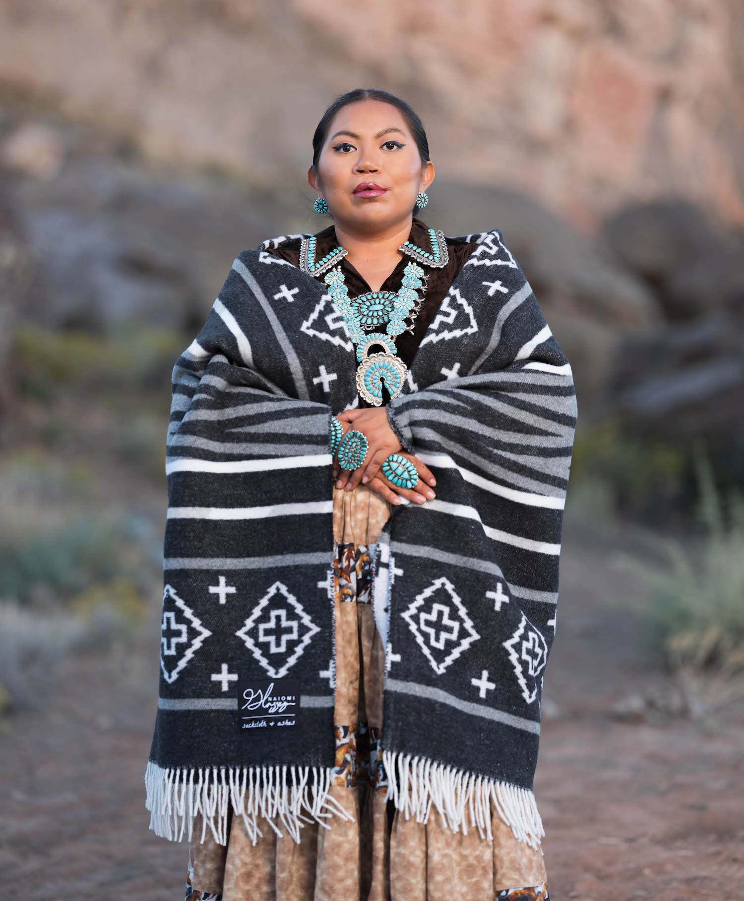Woman wearing a black and white patterned shawl with turquoise jewelry in a natural setting.