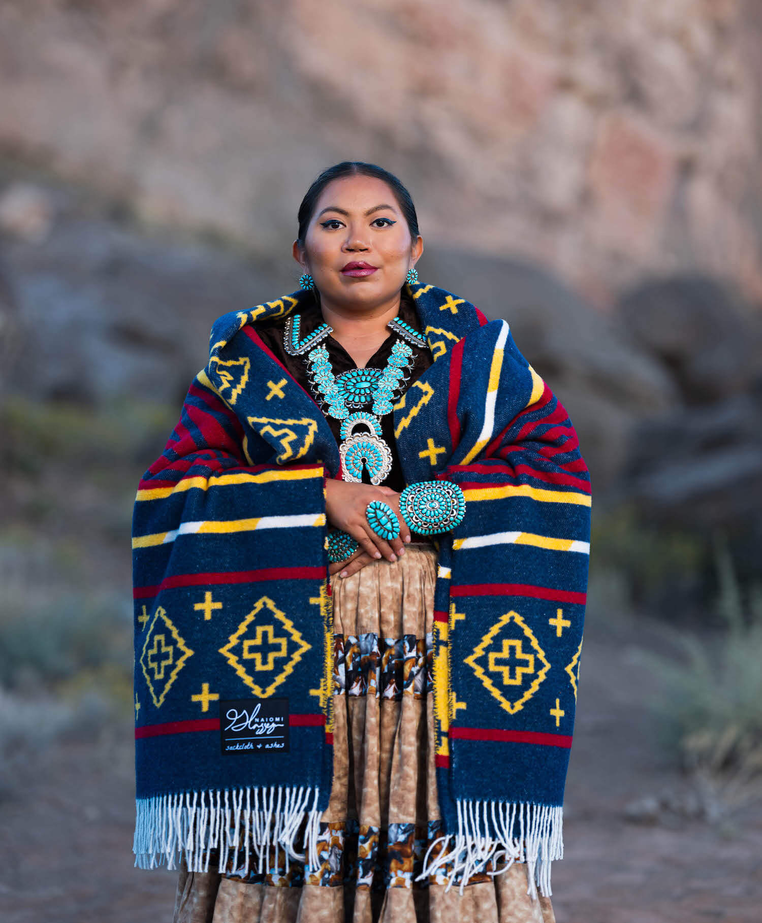 Person wearing a colorful patterned shawl with turquoise jewelry against a natural background