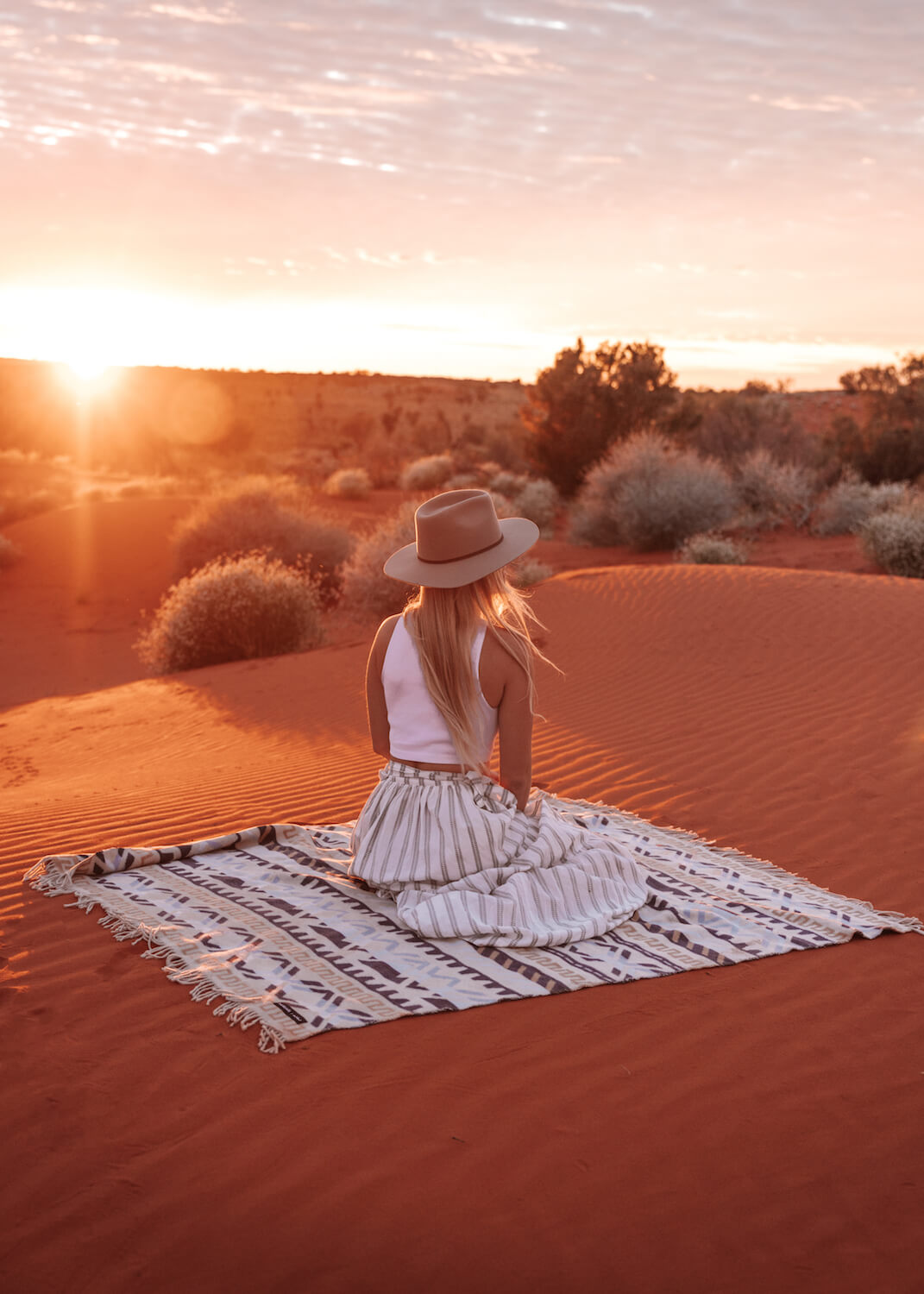 Woman sitting on a blanket in the desert at sunset