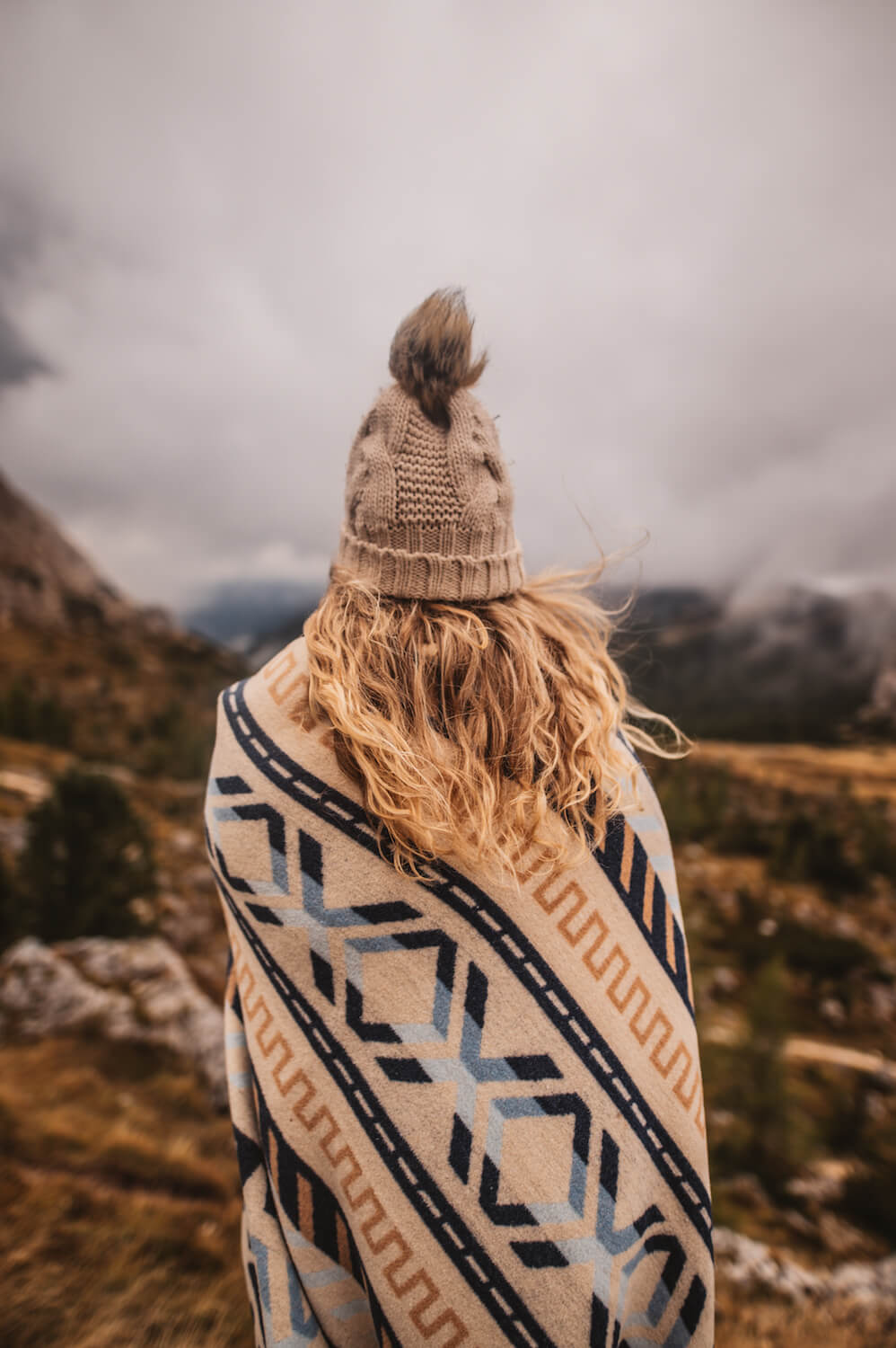 Person wrapped in a patterned blanket with mountains in the background